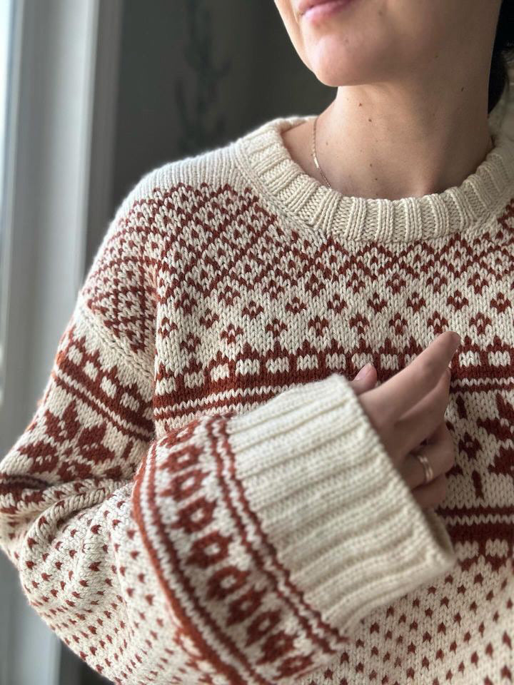 A woman in a colorwork sweater with her hand resting against her heart.