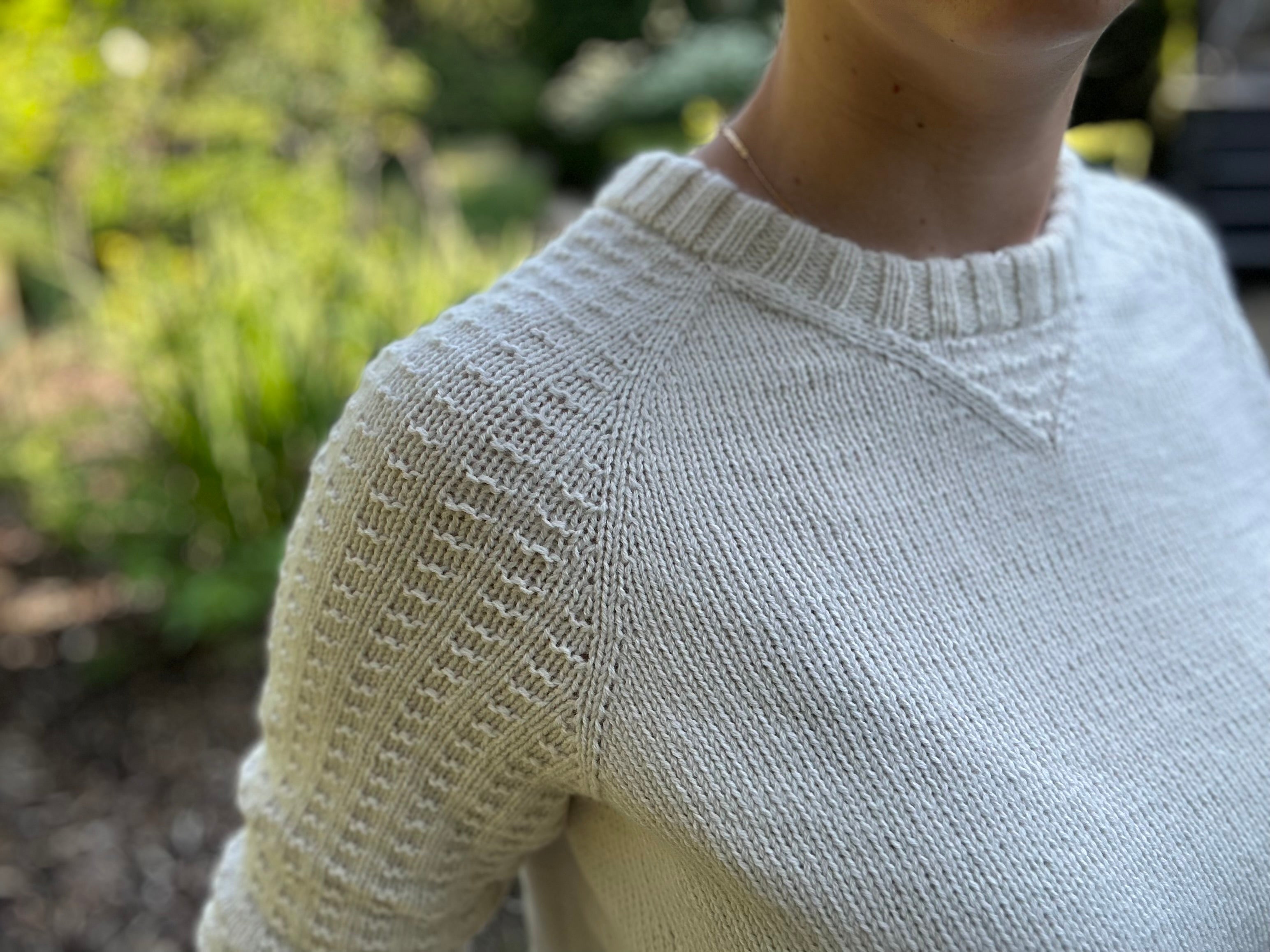 White Raglan pullover with waffle textured sleeves and a textured detail at the center front neck.